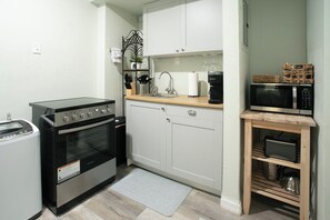 Eine kompakte Küche mit ein eingebautem Backofen, einer Mikrowelle und einer kleinen Holzablage.