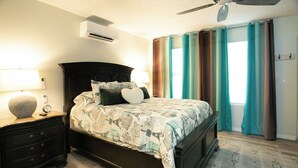 Quarto com cama, mesa de cabeceira, luminária, aparelho de ar condicionado e cortinas.