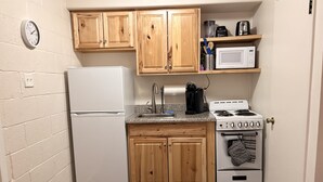 A compact kitchen with wooden cabinets, a white refrigerator, a stove, and a microwave. - Fine Studio Nine @ Rustic Ridge in Granite Dells (Prescott)