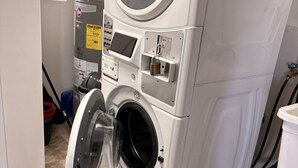 A front-loading washing machine with a control panel, a window with blinds, and a tiled floor. - Fine Studio Nine @ Rustic Ridge in Granite Dells (Prescott)