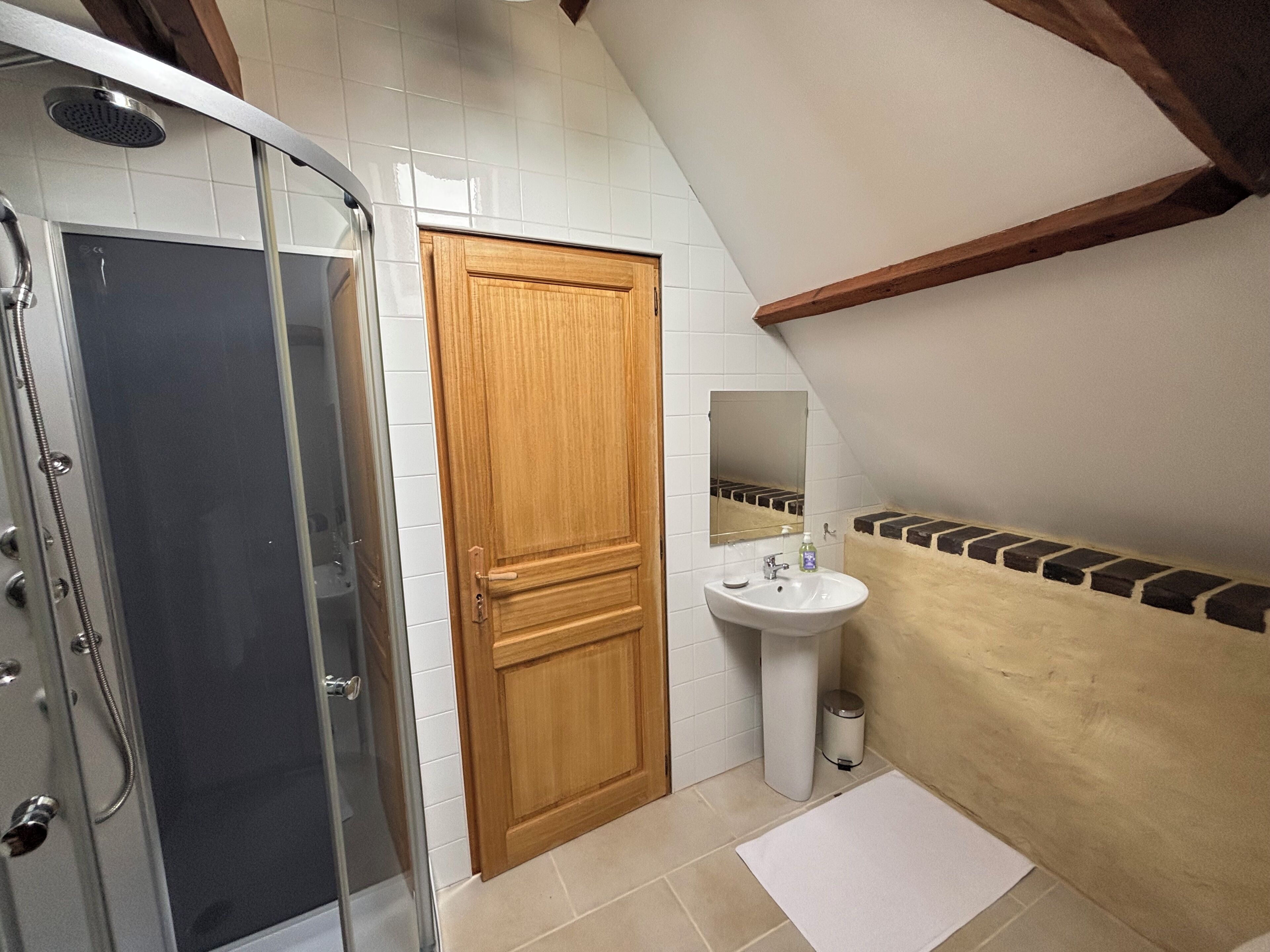 Une salle de bain avec une douche, un lavabo, un miroir et une porte en bois.