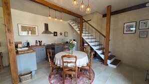 Een keuken met houten kastjes, een eettafel met stoelen, een trap en hanglampen.