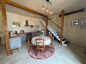 A kitchen with wooden cabinets, a dining table with chairs, a staircase, and pendant lights. - 2-bedroom cottage close to D-Day Beaches and Bayeux at the historic Maison Neuve (Le Molay-Littry)
