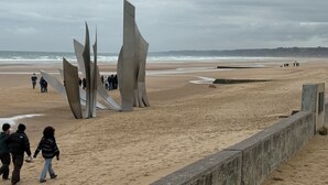 Een strand met abstracte sculpturen, een zandstrand en een vergezicht op zee.