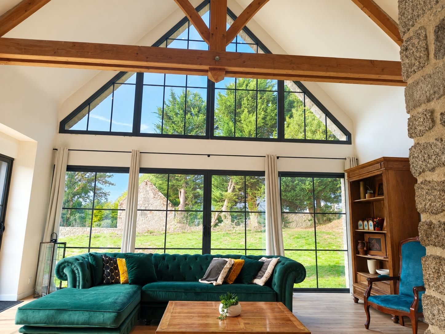 A spacious room with a large window, a green sofa, a wooden coffee table, and a stone wall.