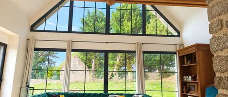 A spacious room with a large window, a green sofa, a wooden coffee table, and a stone wall.