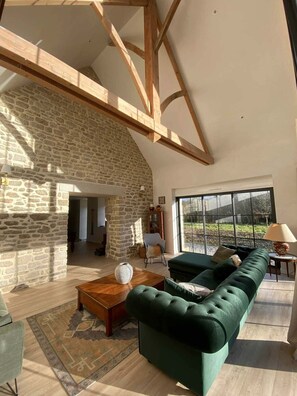 Ein geräumiges Wohnzimmer mit Steinwand, Holzbalken, einem grünen Sofa und einem großen Fenster.