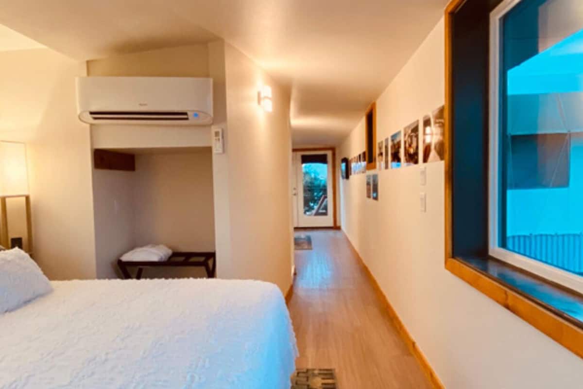 Une chambre d’hôtel comprenant un lit, un bureau, un appareil de climatisation, une fenêtre avec vue et un couloir agrémenté d’un tapis.