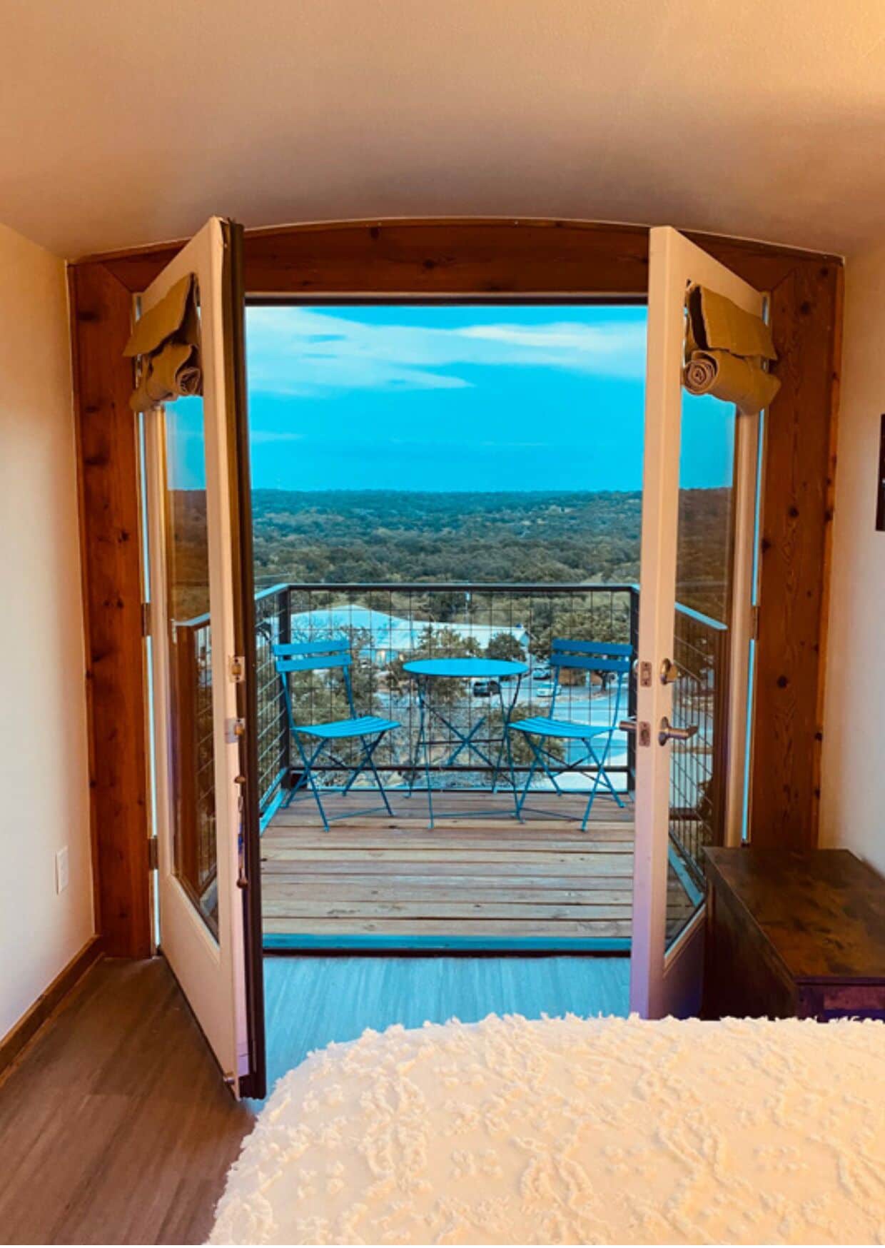 A room with a balcony, wooden doors, and a view of a distant landscape.