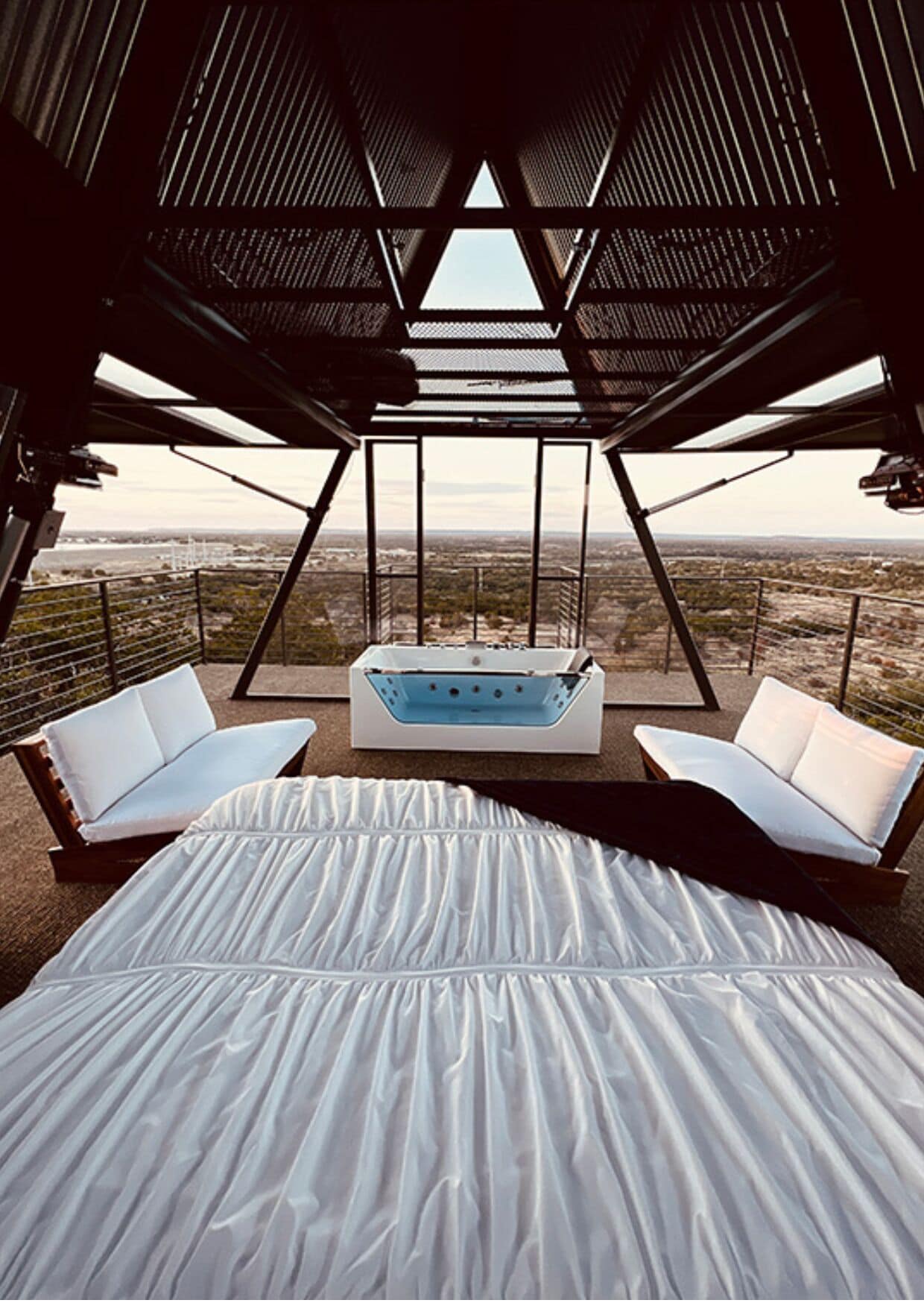 Een kamer met een bed, twee witte slaapbanken, een blauw jacuzzi en uitzicht op een woestijnlandschap.
