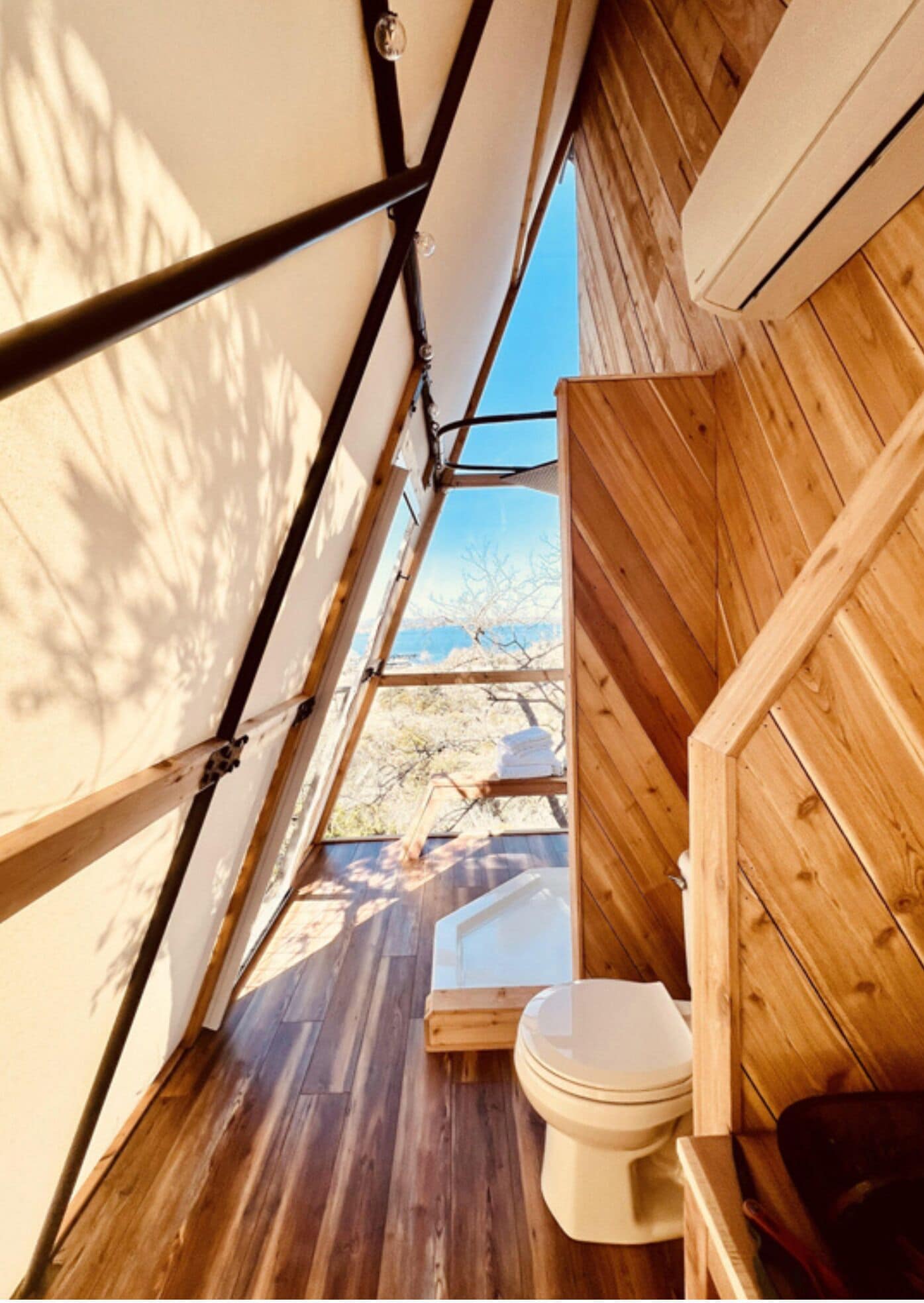 A wooden interior with a toilet, a bench, and a window overlooking a mountainous landscape.