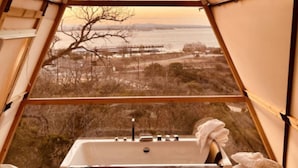 Una tenda con vasca da bagno, un letto e vista sul paesaggio.