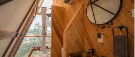 Une cabane en bois avec un toit en pente, des toilettes, un lavabo avec un receveur, un appareil de climatisation et une serviette suspendue à un porte-serviettes.