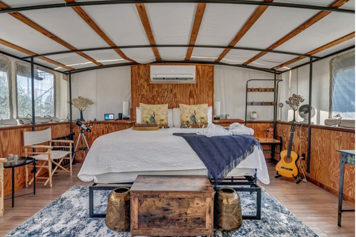 Une chambre spacieuse avec un grand lit, des éléments décoratifs en bois, un bureau et une guitare.