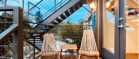 Une terrasse en bois avec deux chaises et une table en bois, une rambarde en verre et un escalier.