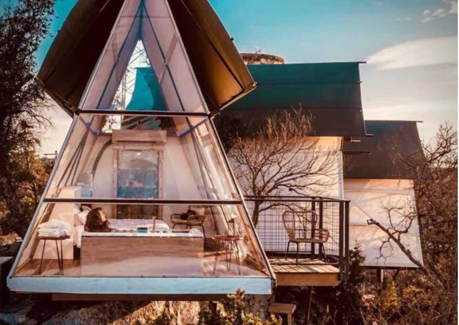 A geodesic dome structure with a glass floor, a bed, and a chair.