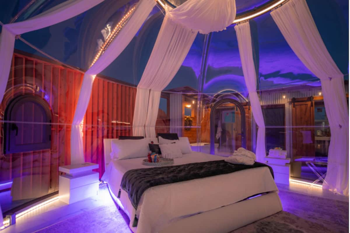 Une chambre à coucher luxueuse avec un lit à baldaquin, une salle de bain entièrement vitrée et une vue sur l’extérieur.