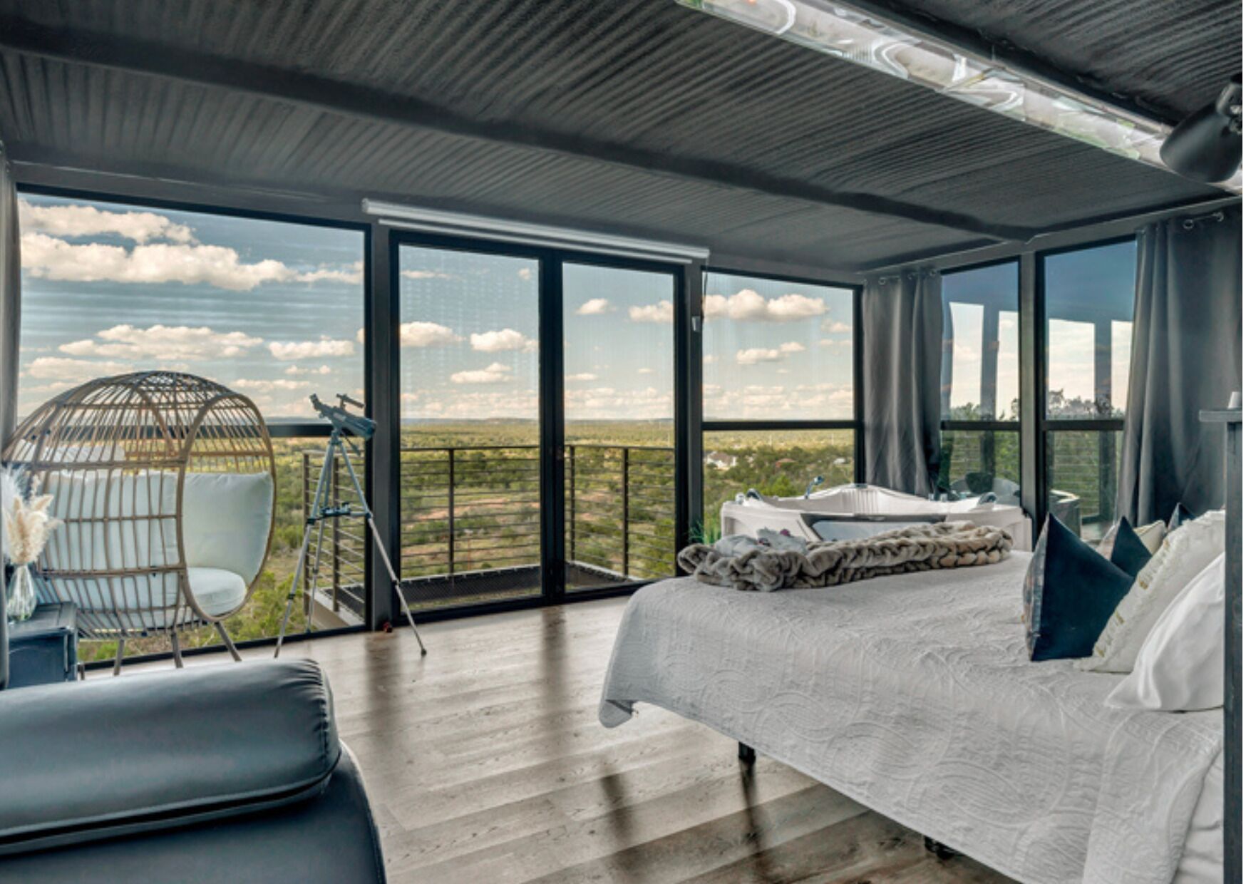 Una camera da letto con un letto grande, una sedia, un telescopio e un balcone vista paesaggio.