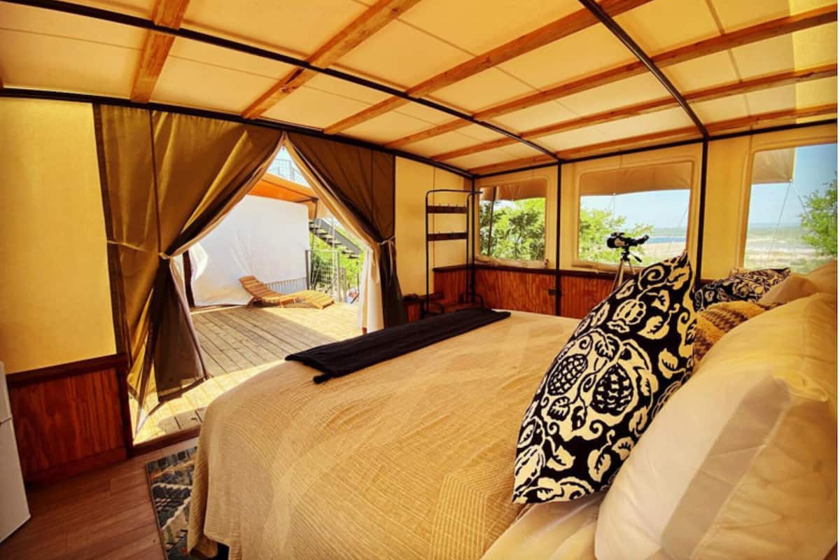 Un hébergement sous tente comprenant un lit, une vue sur l’extérieur et une terrasse en bois.