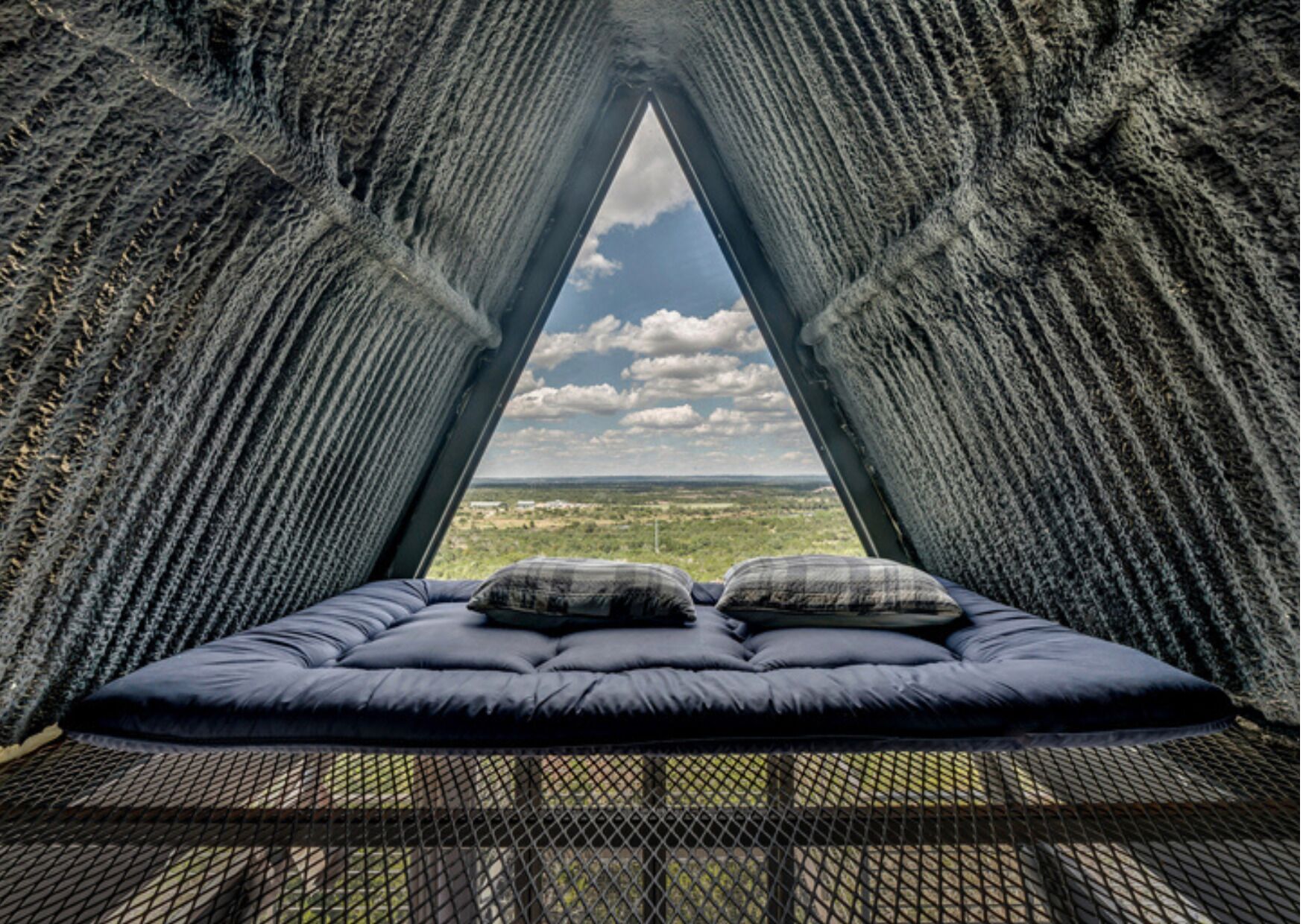 A room with a bed, a view through a triangular window, and a textured wall.