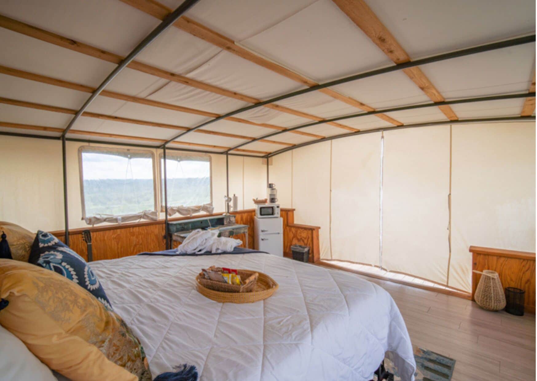 A tented room with a bed, a small desk, a window, and a view of the outdoors.