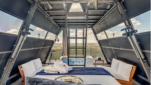 Una stanza triangolare con un letto, un tavolino e una finestra che si affaccia sul paesaggio.