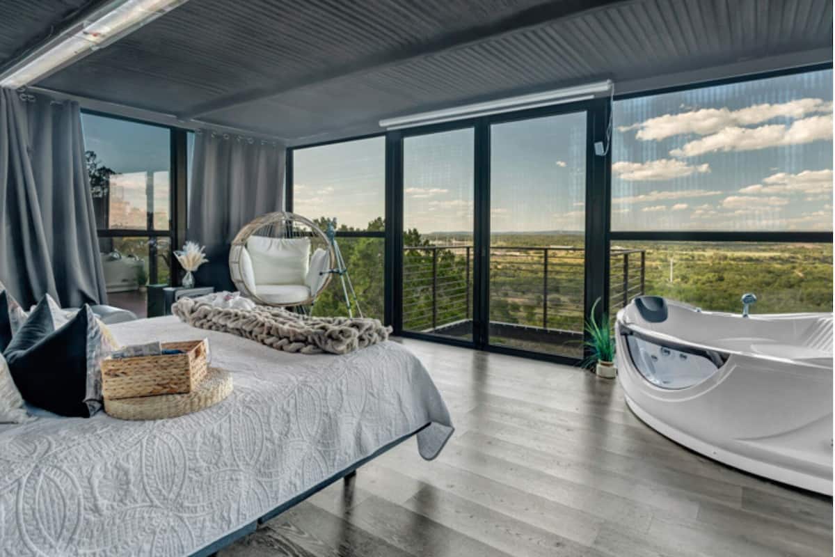 Une chambre avec un grand lit, un fauteuil suspendu, une baignoire et un balcon avec vue.