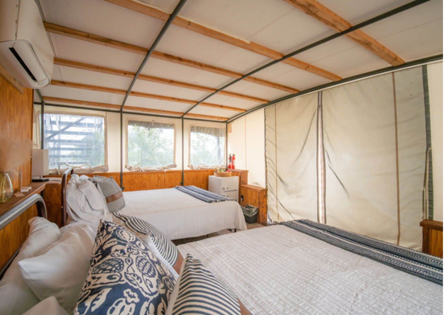 Una cabaña con dos camas, techo de madera, una ventana y una cortina.