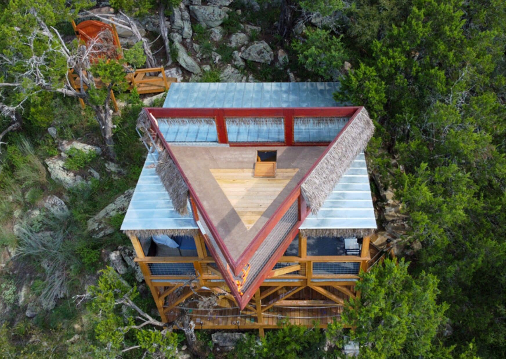 A triangular wooden structure with a flat roof, surrounded by dense green foliage.