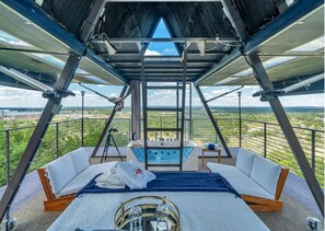 Ein Zimmer mit hohen Decken, einem Bett, einem kleinen Tisch mit Gläsern und Blick auf eine Landschaft.