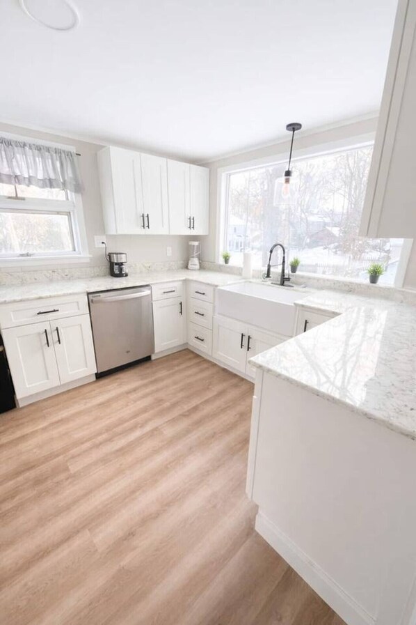 A modern kitchen with white cabinetry, a dishwasher, a coffee maker, and a window with a view of a snowy landscape.