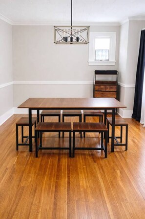 A dining area with a wooden table and benches, a hanging light fixture, and a window with blinds.