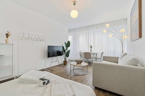A modern, well-lit living room with a sofa, a TV, a dining area, and a large window with curtains. - Modern Studio in Central Luxembourg City (Luxembourg)