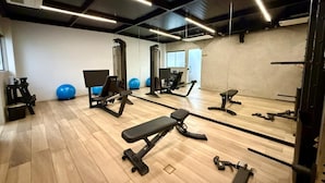 Un gimnasio con equipo de ejercicio, espejos y suelo de madera.