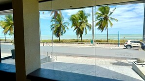 Vista desde una ventana con palmeras y una playa al fondo.