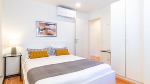 A hotel room with a bed, bedside table, lamp, air conditioning unit, and a door leading to a closet. - B: Douro & Bridge Views | Boutique Apartments (Vila Nova de Gaia)