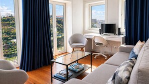 A modern living room with a glass coffee table, a sofa, a desk with a computer and TV, and large windows with curtains. - B: Douro & Bridge Views | Boutique Apartments (Vila Nova de Gaia)