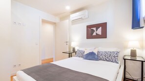 A hotel room with a bed, bedside tables, a wall-mounted air conditioner, and a door leading to another room. - B: Douro & Bridge Views | Boutique Apartments (Vila Nova de Gaia)