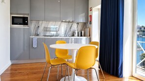 A modern kitchen with a microwave, stove, and sink. There is a dining area with a round table and yellow chairs. - B: Douro & Bridge Views | Boutique Apartments (Vila Nova de Gaia)