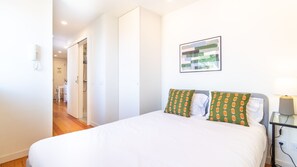 A bedroom with a bed, a bedside table with a lamp, a wall-mounted artwork, and a door leading to a bathroom. - A: Douro & Bridge Views | Boutique Apartments (Vila Nova de Gaia)
