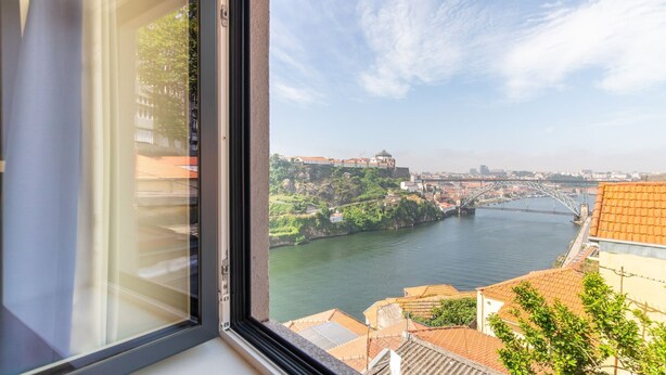 Blick aus einem Fenster auf einen Fluss mit Brücke, Gebäuden und Grünflächen.