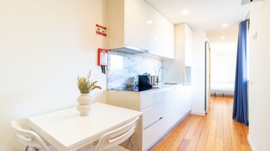 A modern kitchen with white cabinetry, a marble countertop, and a small dining table with a vase of dried flowers. - A: Douro & Bridge Views | Boutique Apartments (Vila Nova de Gaia)