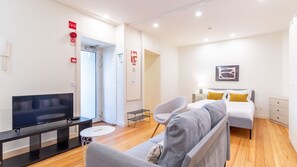 Ein modernes Hotelzimmer mit Fernseher, einer Couch, einem Bett mit gelben Kissen und einem kleinen Beistelltisch.