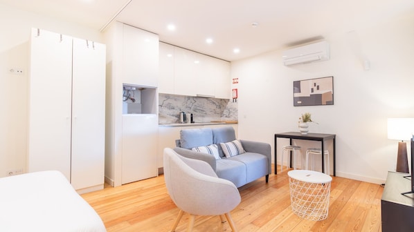 A modern living room with a sofa, a round coffee table, a small side table, and a kitchen area with a marble backsplash. - C: Douro & Bridge Views | Boutique Apartments (Vila Nova de Gaia)