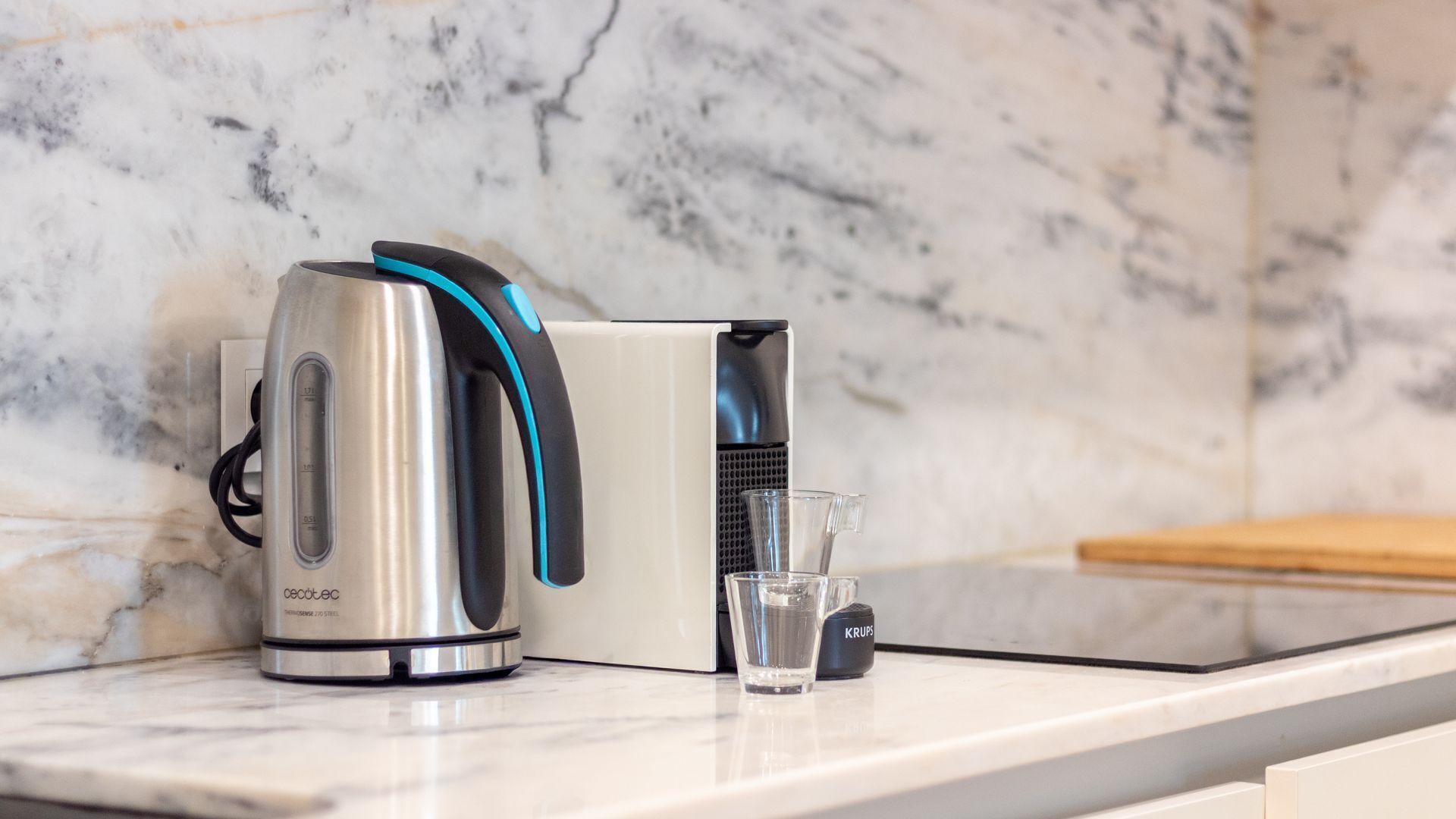 Cozinha com chaleira, copo e cafeteira em bancada de mármore.