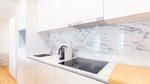 A modern kitchen with white cabinetry, a marble backsplash, and a stainless steel sink. - C: Douro & Bridge Views | Boutique Apartments (Vila Nova de Gaia)