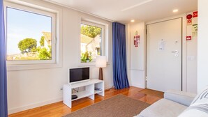 Ein Zimmer mit Fernseher auf einem weißen Schrank, einer Tür mit Sicherheitshinweis und einem Fenster mit Blick auf Grünflächen.