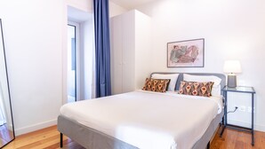 Ein Hotelzimmer mit einem Bett, einem Nachttisch mit Lampe, einem Gemälde an der Wand und einer Tür zu einem anderen Raum.