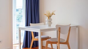 A dining area with a white table, two chairs, a vase with dried flowers, and a view through a window with blue curtains. - D: Sunset Douro & Ponte Luis I Views (Vila Nova de Gaia)