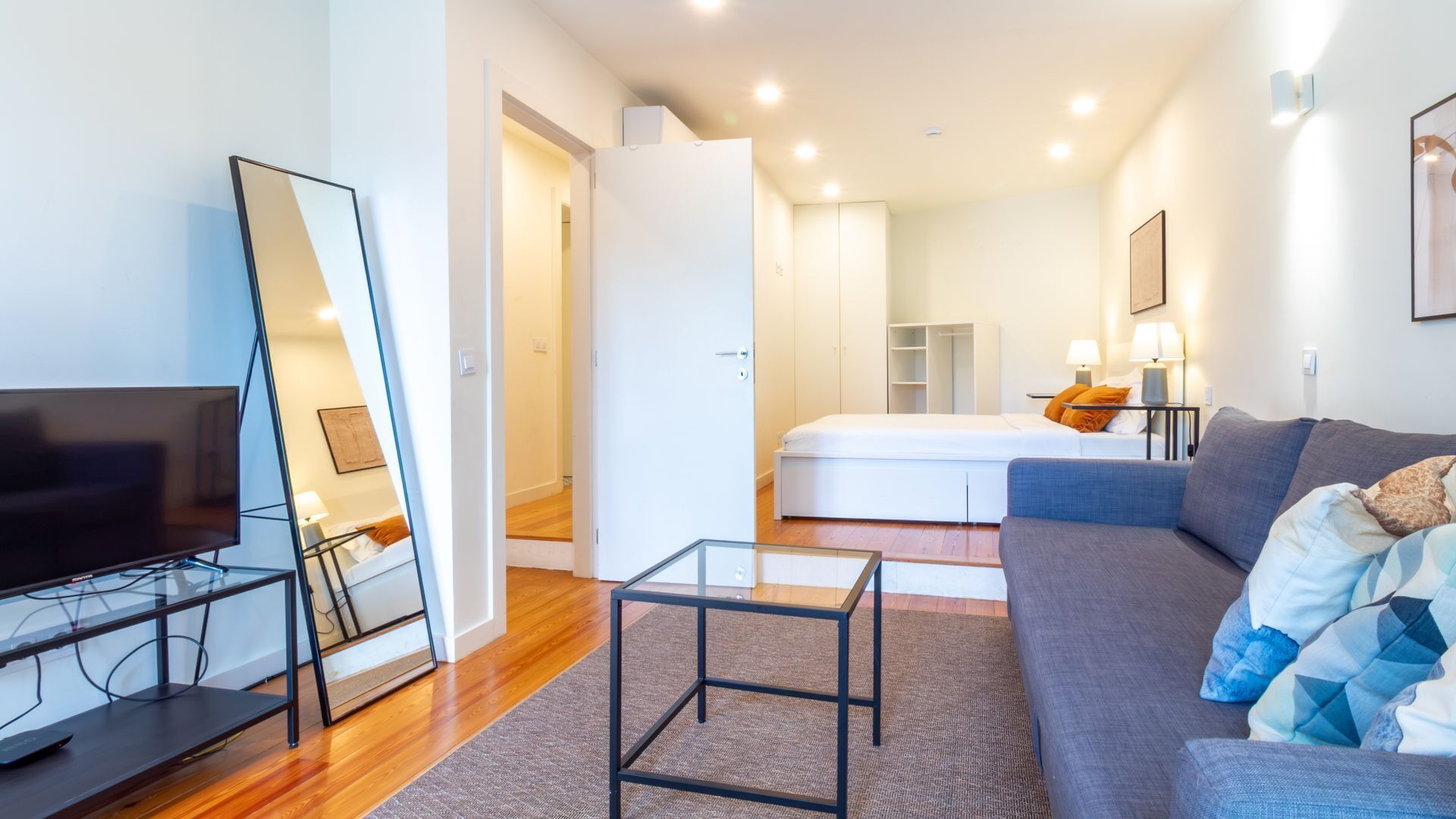A modern hotel room with a TV, a glass coffee table, a sofa, a bed, and a wardrobe.
